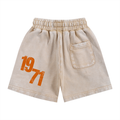 Beige denim shorts with an orange distressed '1971' graphic on the left leg and a back pocket, shown on a plain white background.